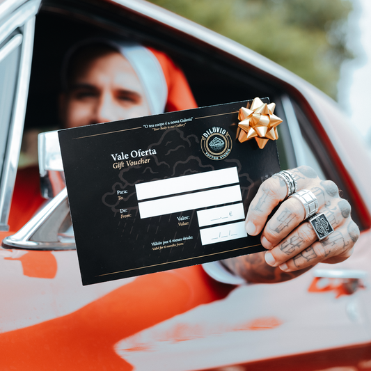 Pessoa a segurar um gift voucher do Dilúvio Tattoo Studio pela janela de um carro, destacando o cartão oferta preto com logótipo do estúdio de tatuagens em Lisboa