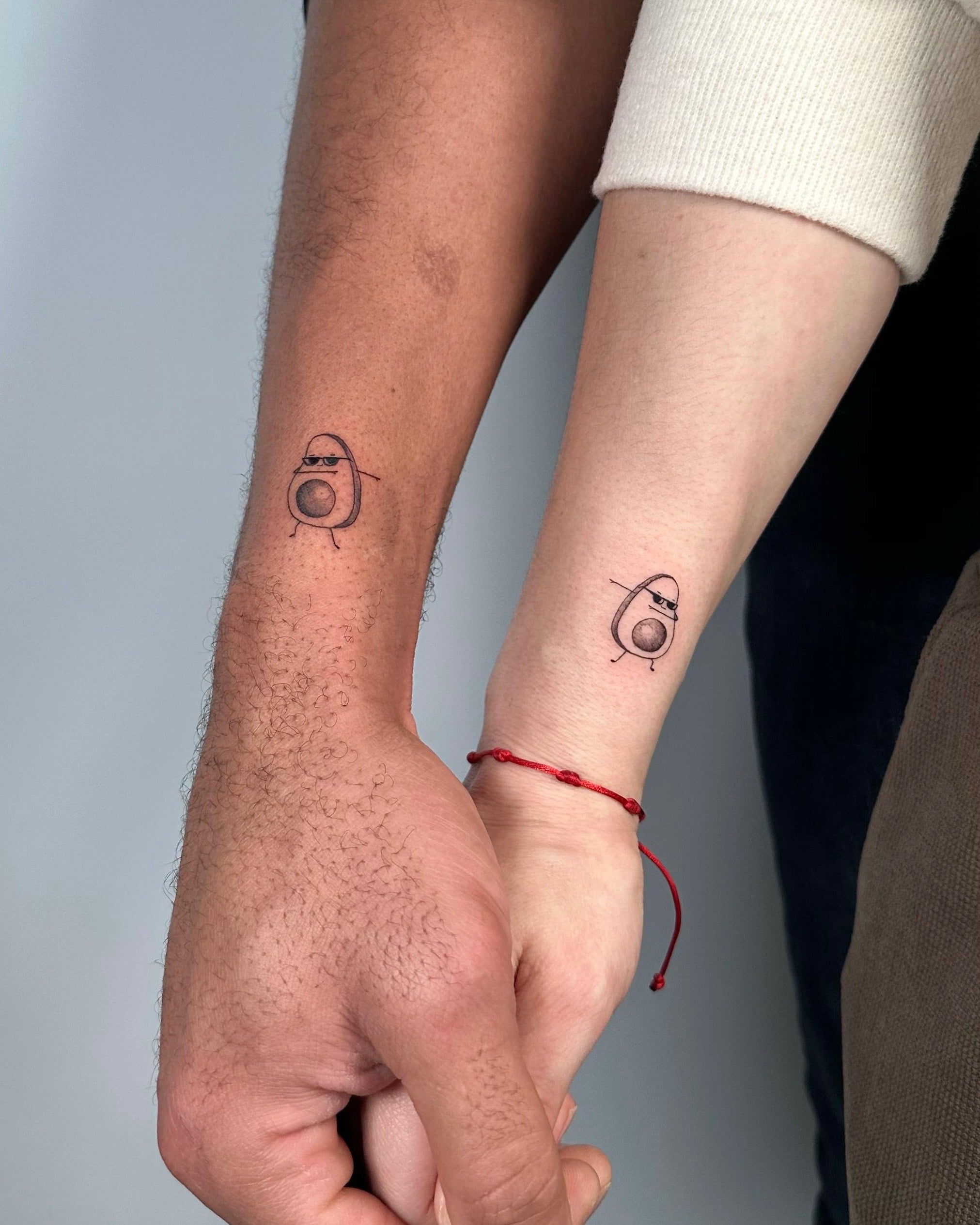 tatuagens fine line matching de doiss pequenis abacates nos pulsos de casal, estilo simbólico minimalista, no Dilúvio Tattoo em Benfica.