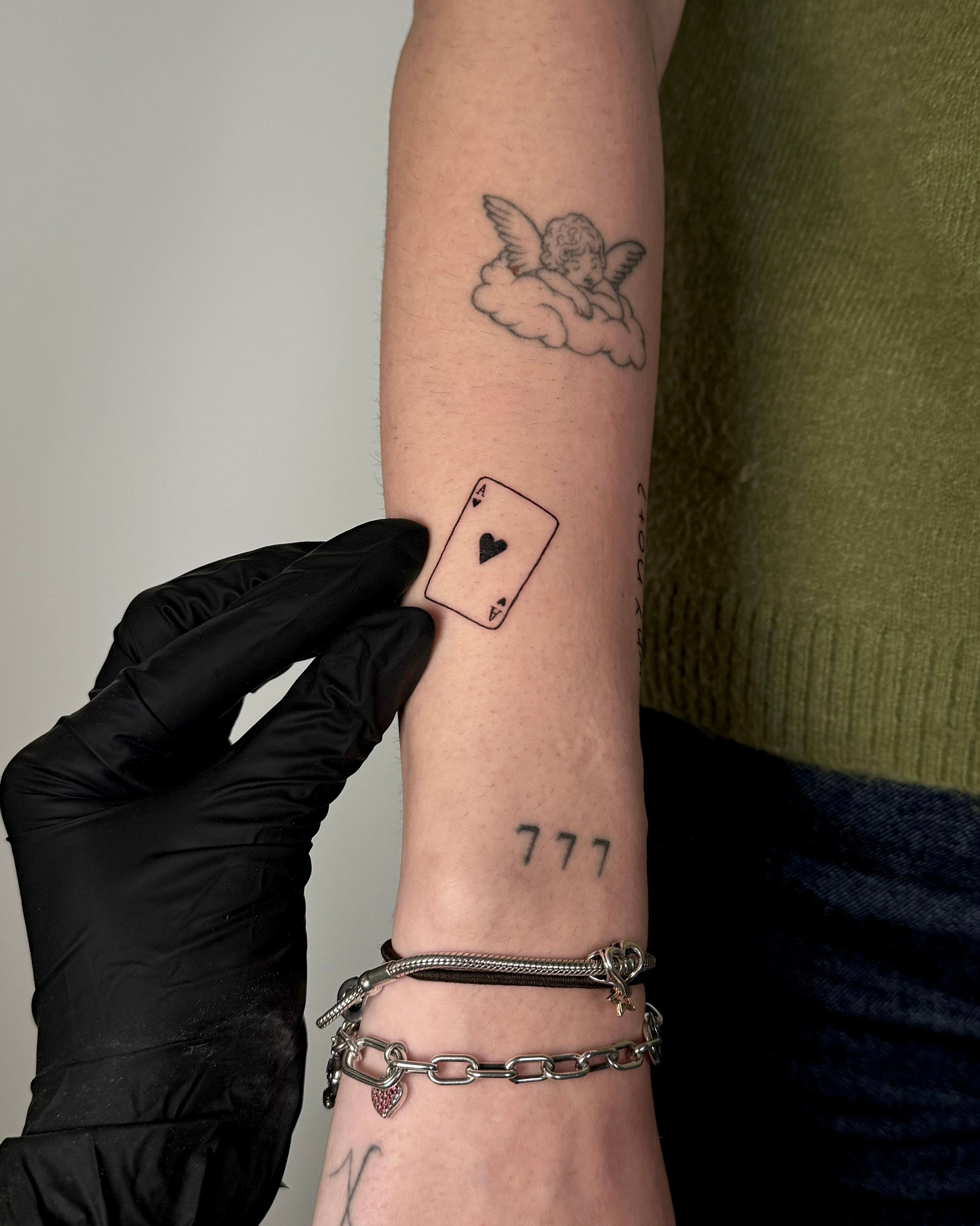 Composição fine line de carta de ás de espadas e número 777 no antebraço, estilo simbólico minimalista, no Dilúvio Tattoo em Benfica.