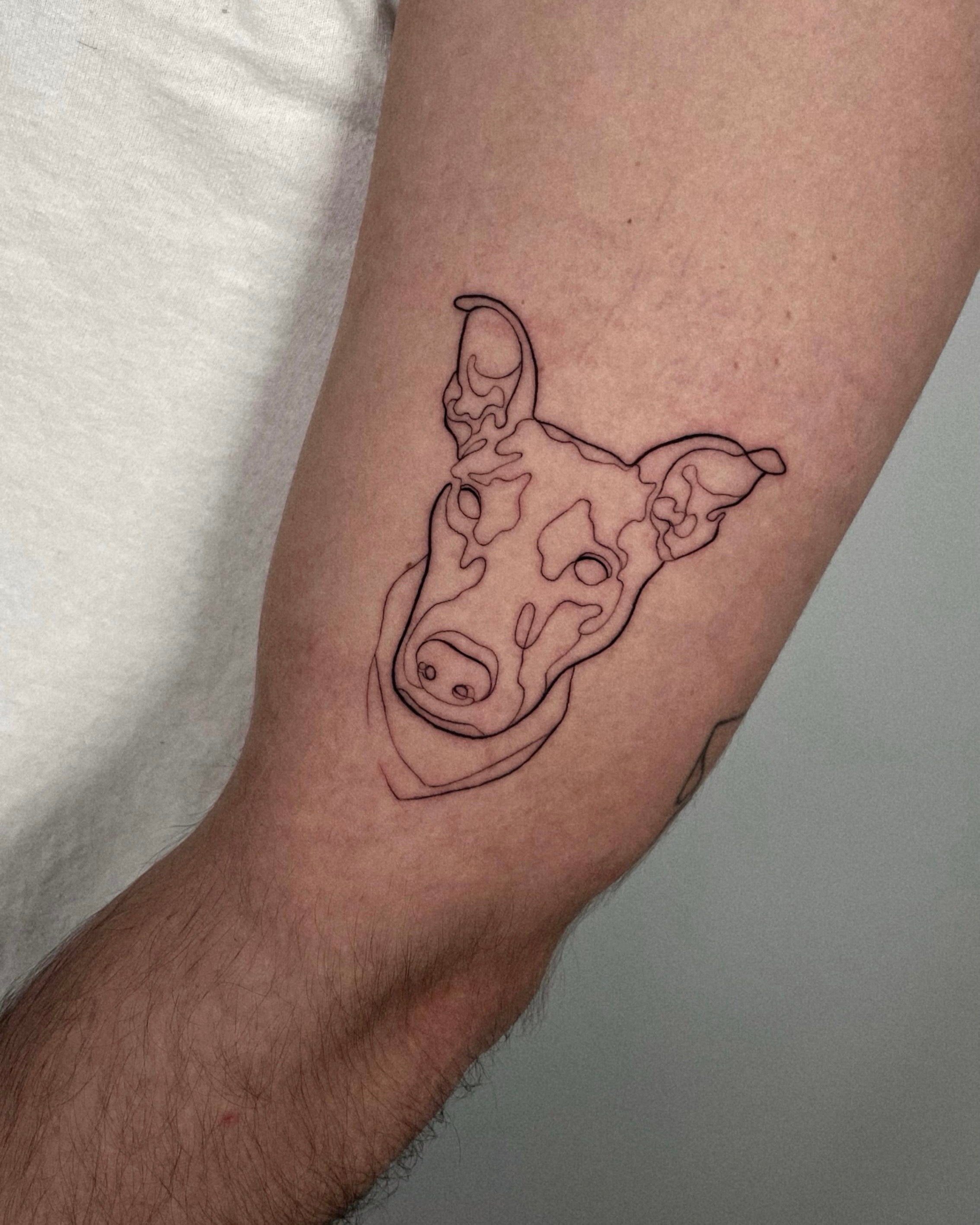 Tatuagem fine line de cabeça de cão em técnica de linha contínua no braço, estilo ilustrativo dedicado ao animal de estimação, no Dilúvio Tattoo em Benfica.