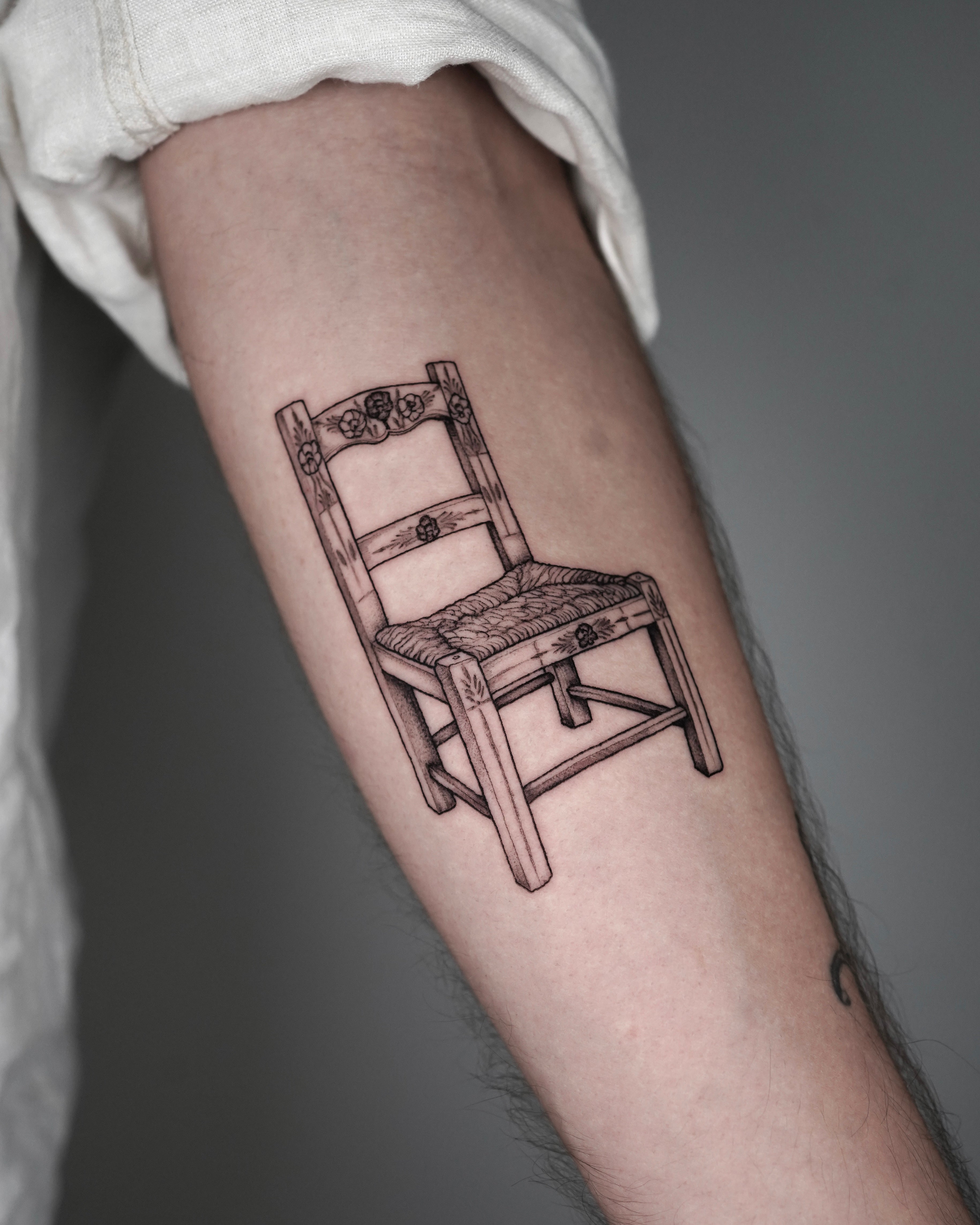 Tatuagem fine line com pontilhismo de cadeira alentejana tradicional portuguesa com flores no antebraço, estilo cultural lusitano, no Dilúvio Tattoo em Benfica.