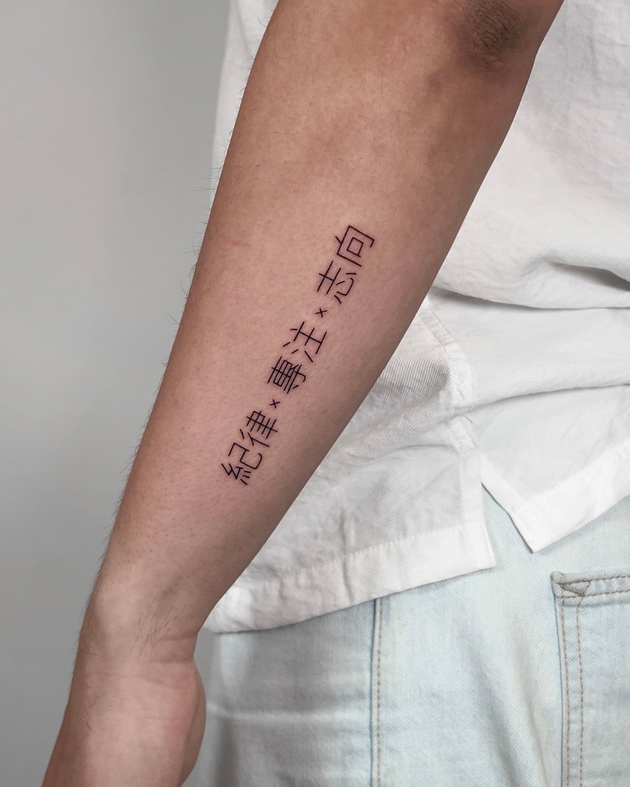 Tatuagem fine line de caracteres orientais em vertical no antebraço, estilo lettering minimalista, feita no Dilúvio Tattoo em Benfica, Lisboa.