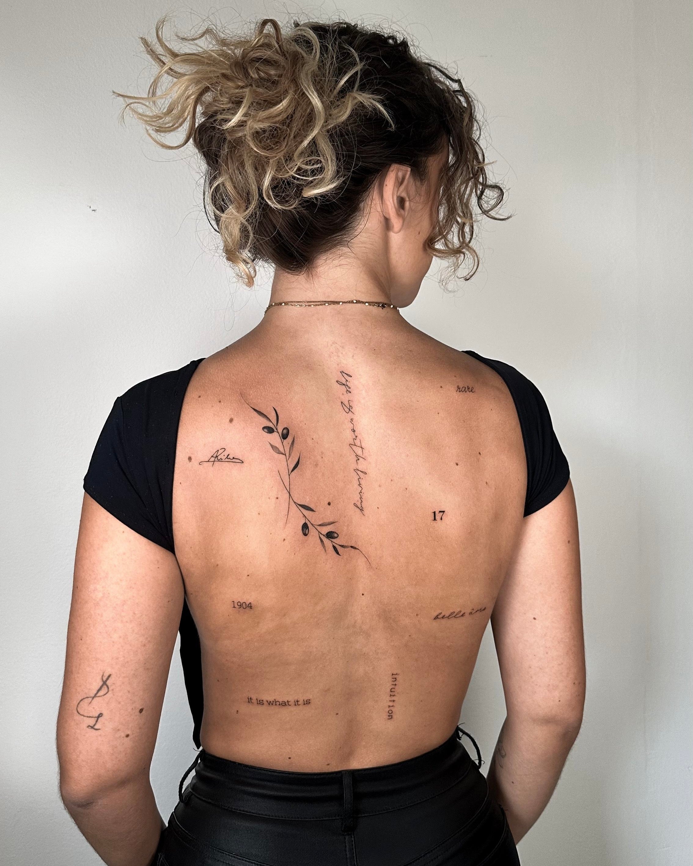 composição de várias tatuagens fine line nas costas com ramo, lettering, frases e números, estilo minimalista simbólico, no Dilúvio Tattoo em Benfica.
