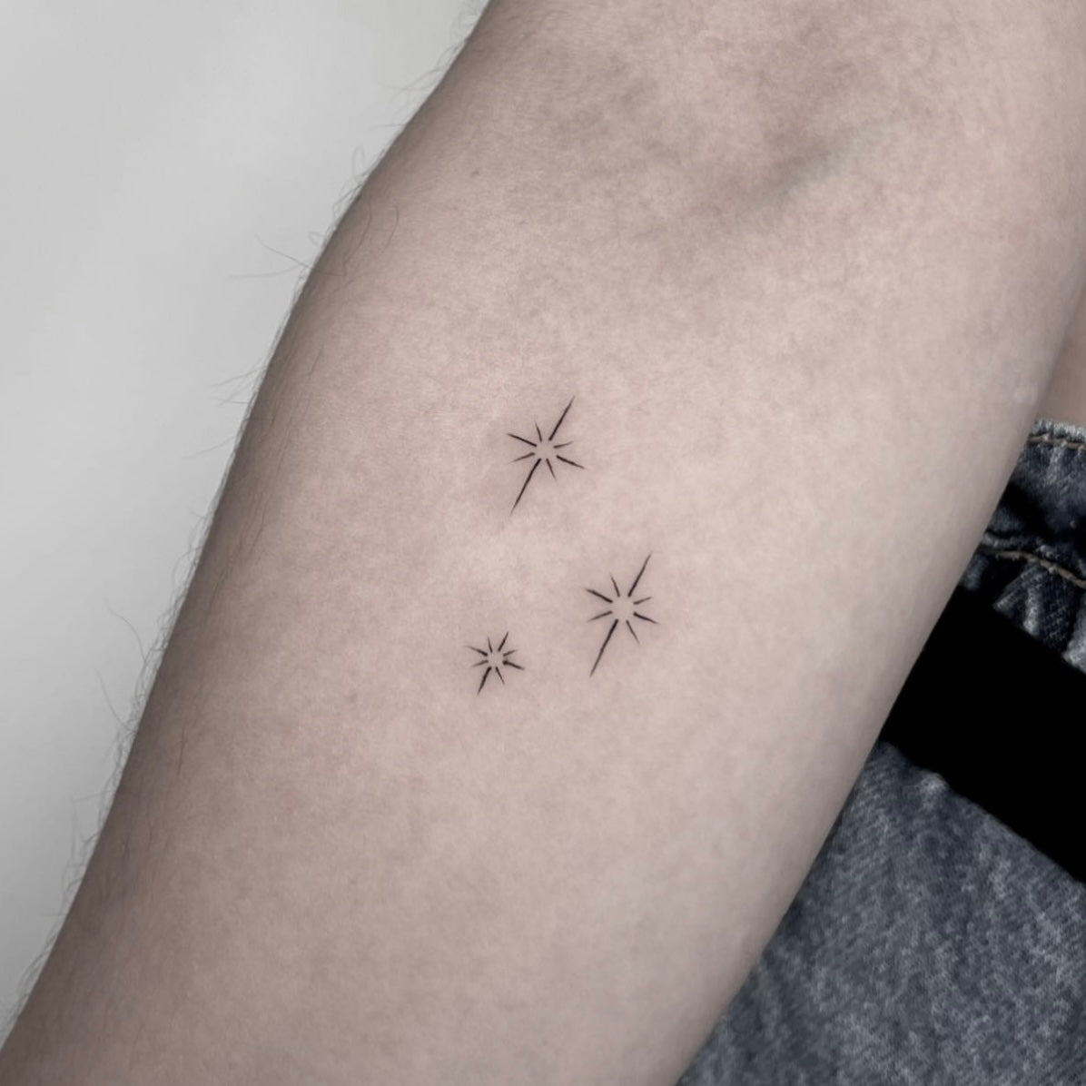 Tatuagem fine line de pequenas estrelas em constelação no braço, estilo minimalista astronómico, no Dilúvio Tattoo em Benfica.