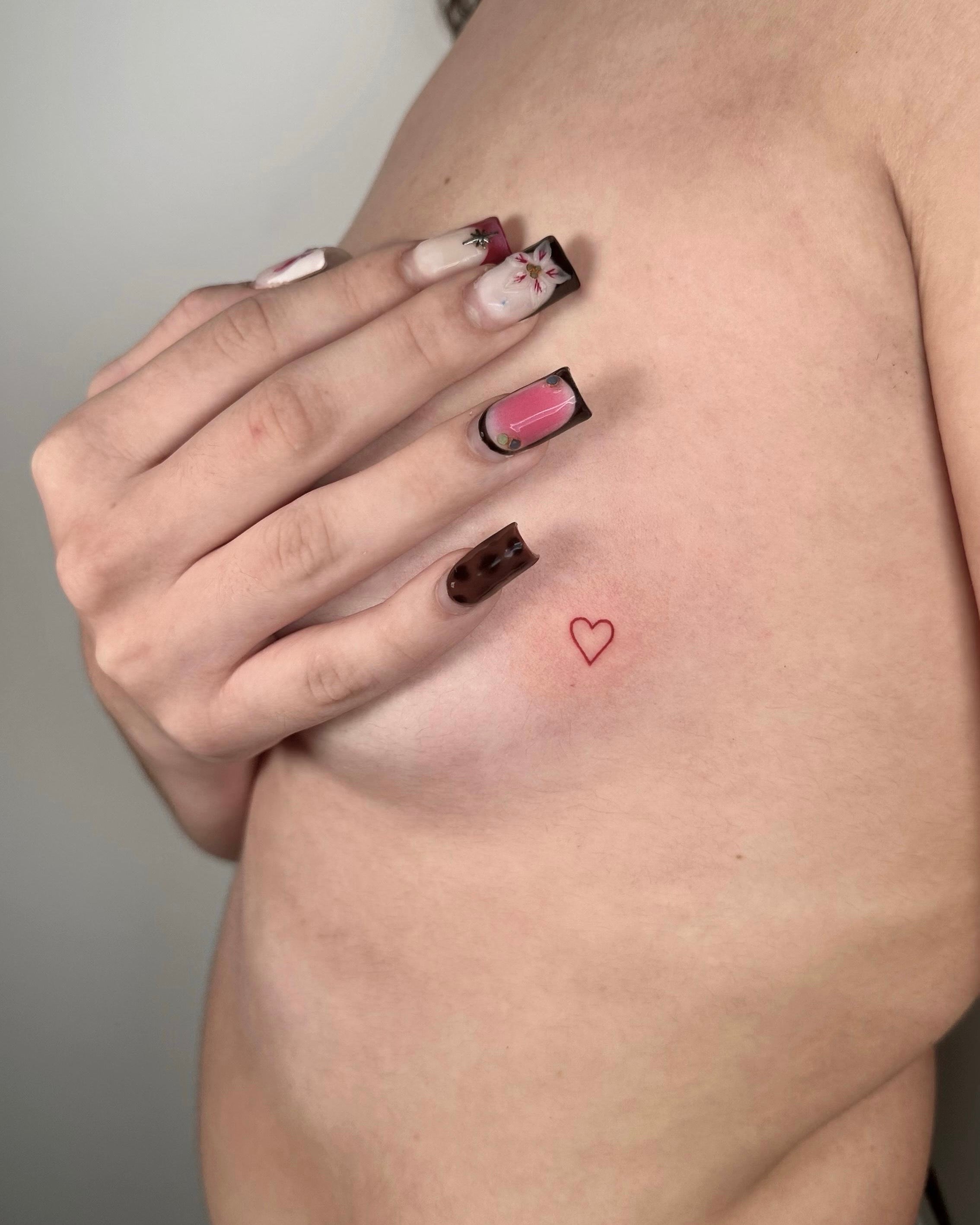 Tatuagem fine line de coração vermelho pequeno na anca, estilo minimalista feminino, no estúdio Dilúvio em Benfica, Lisboa.