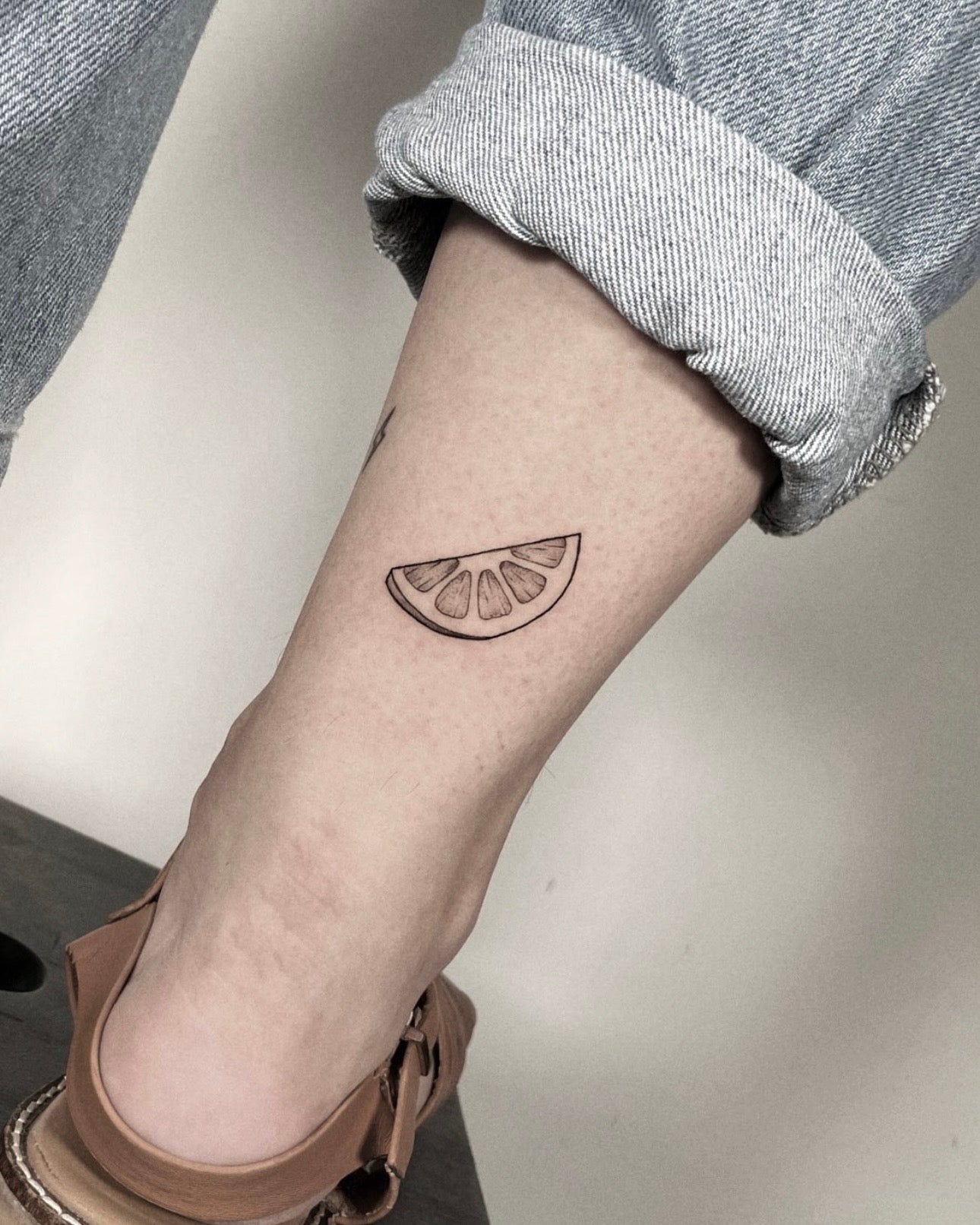 Tatuagem fine line de fatia de limão no braço, estilo minimalista simples, feita no Dilúvio Tattoo em Benfica, Lisboa.