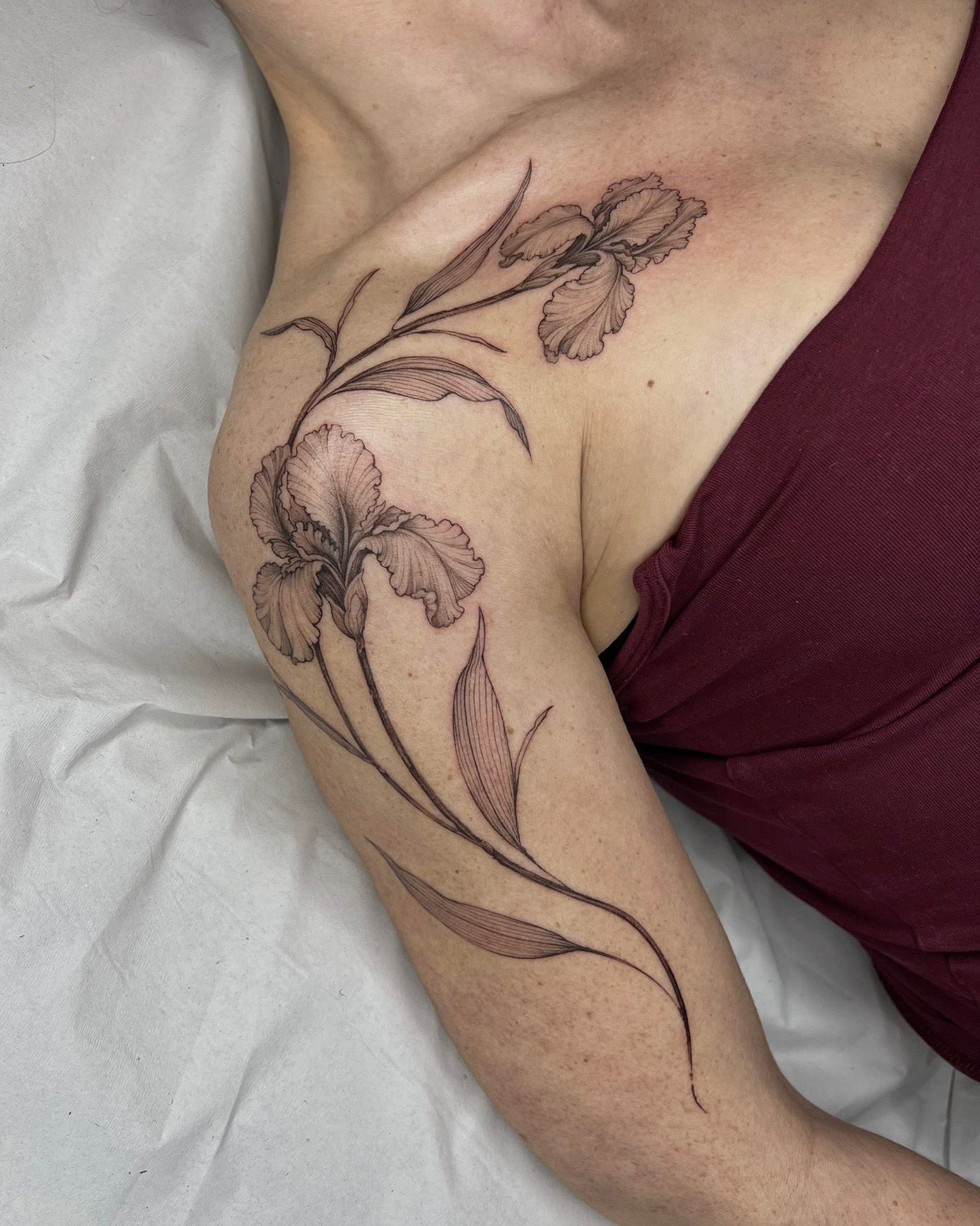 Tatuagem fine line de flor íris com folhas alongadas do ombro ao braço, estilo botânico feminino com sombreado delicado, no Dilúvio Tattoo em Benfica