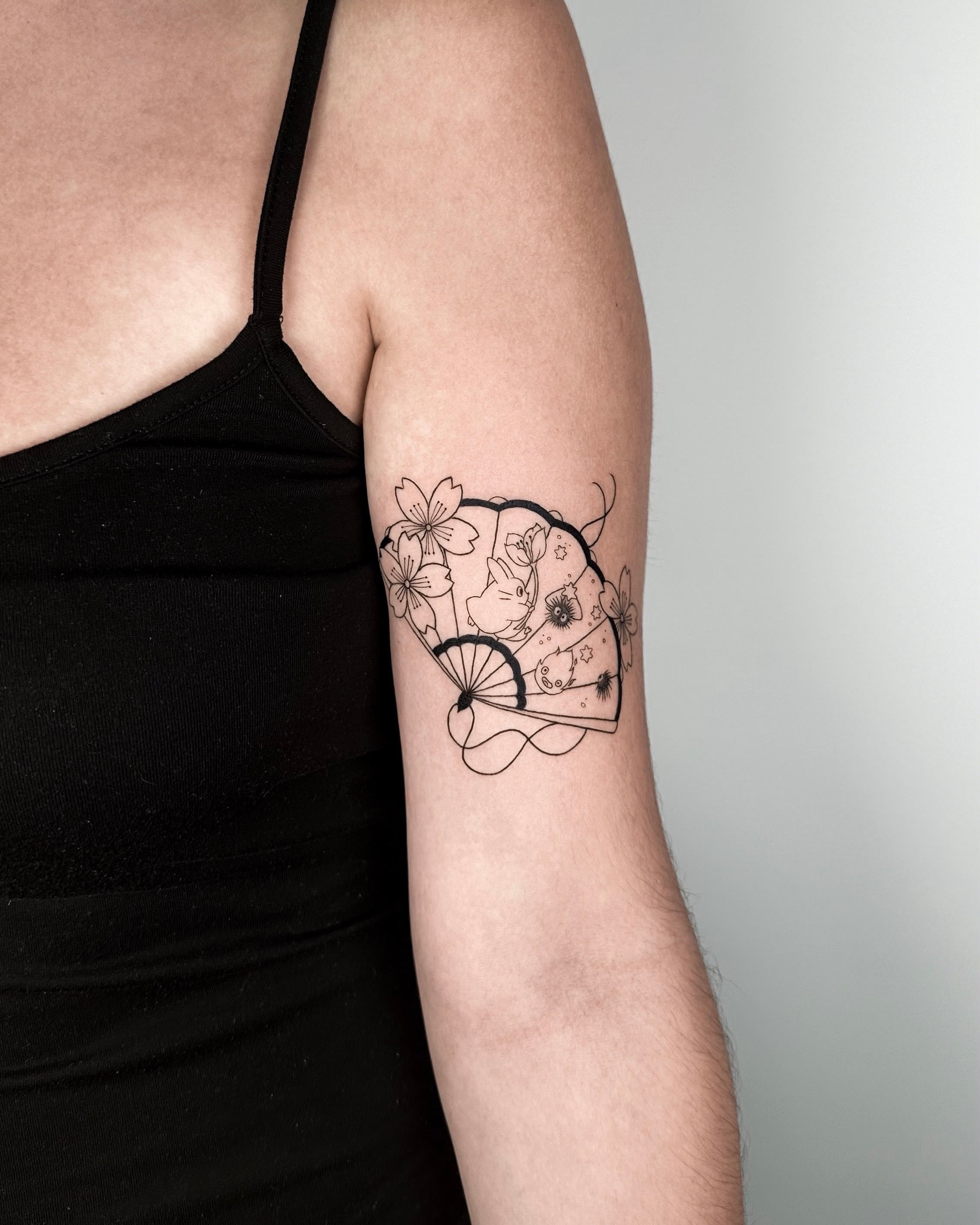 Tatuagem fine line de leque japonês com flores e ramo no braço, estilo oriental delicado feminino, no Dilúvio Tattoo em Benfica.