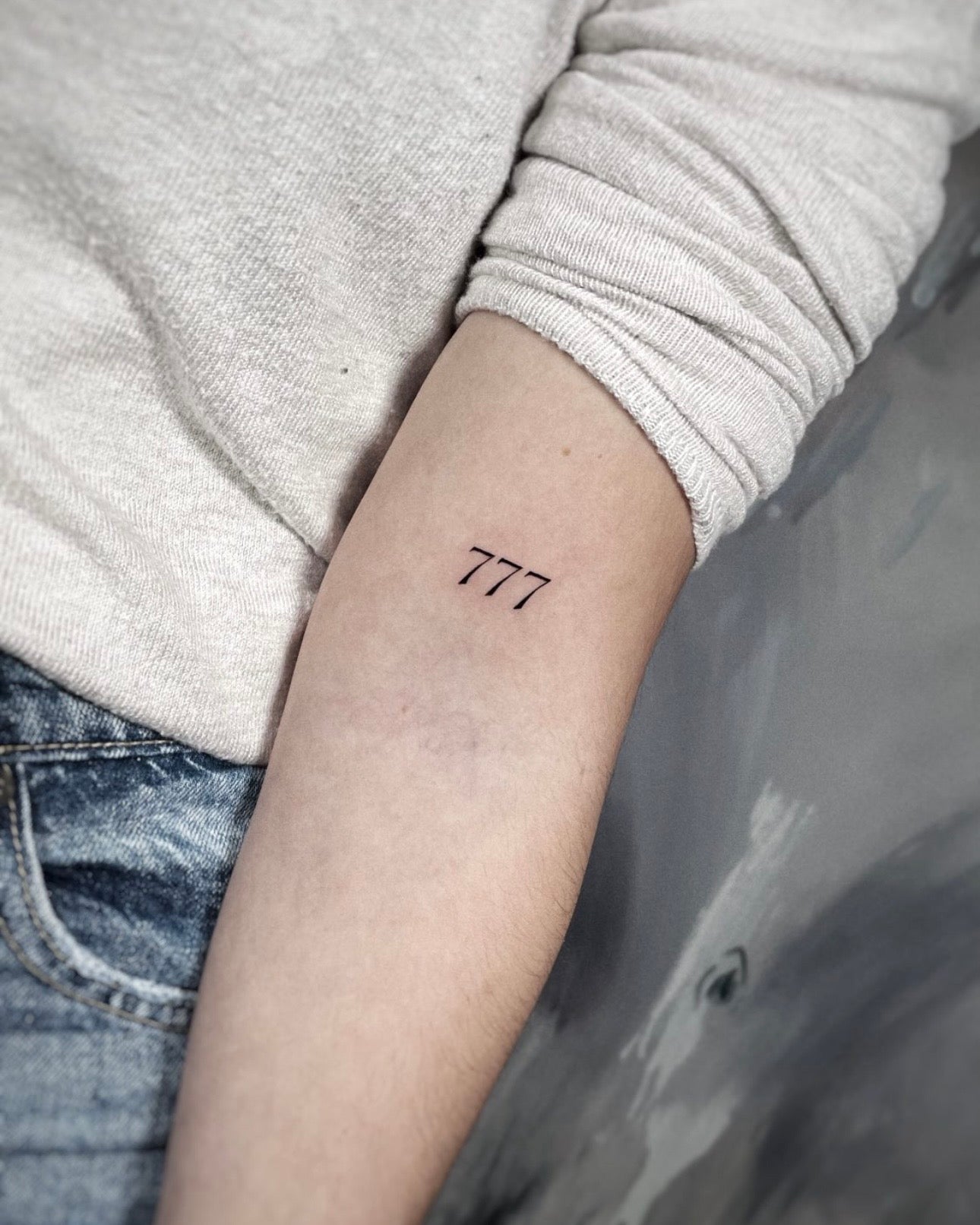 Tatuagem fine line de números 777 (número angelical) no braço, estilo minimalista, feita no Dilúvio Tattoo em Benfica, Lisboa.