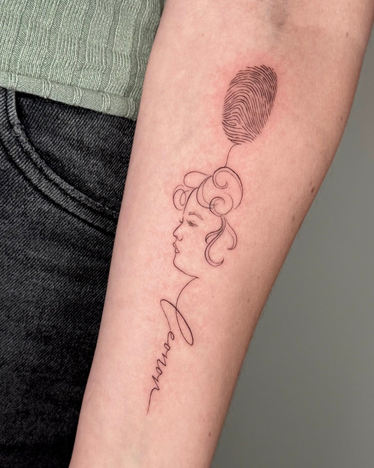 Tatuagem fine line de perfil feminino a segurar balão em forma de impressão digital com lettering de nome no braço, estilo ilustrativo simbólico, no Dilúvio Tattoo em Benfica.