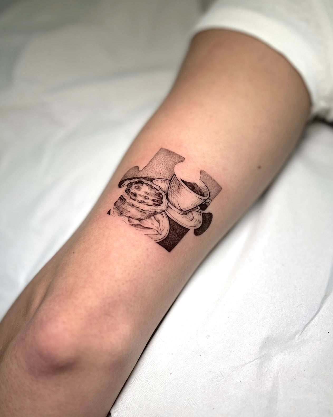 Tatuagem fine line com sombreado de peça de puzzle com chávenas de café empilhadas no braço, estilo ilustrativo, no Dilúvio Tattoo em Benfica.