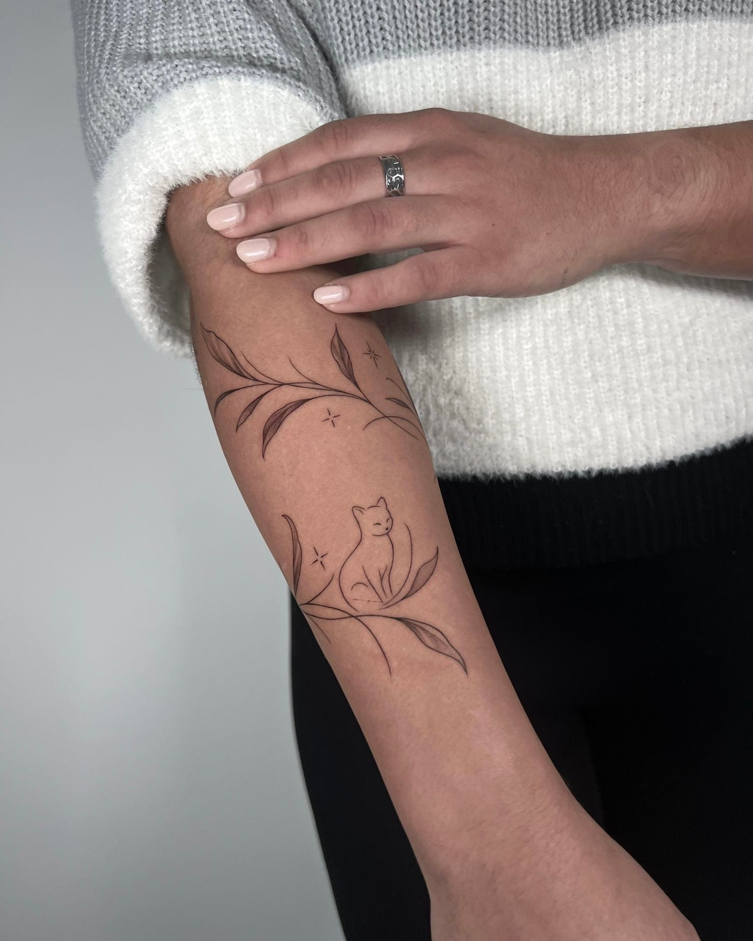 tatuagem fine line de ramo com folhas a envolver o braço com silhueta de gato ao centro, estilo botânico delicado feminino, no Dilúvio Tattoo em Benfica