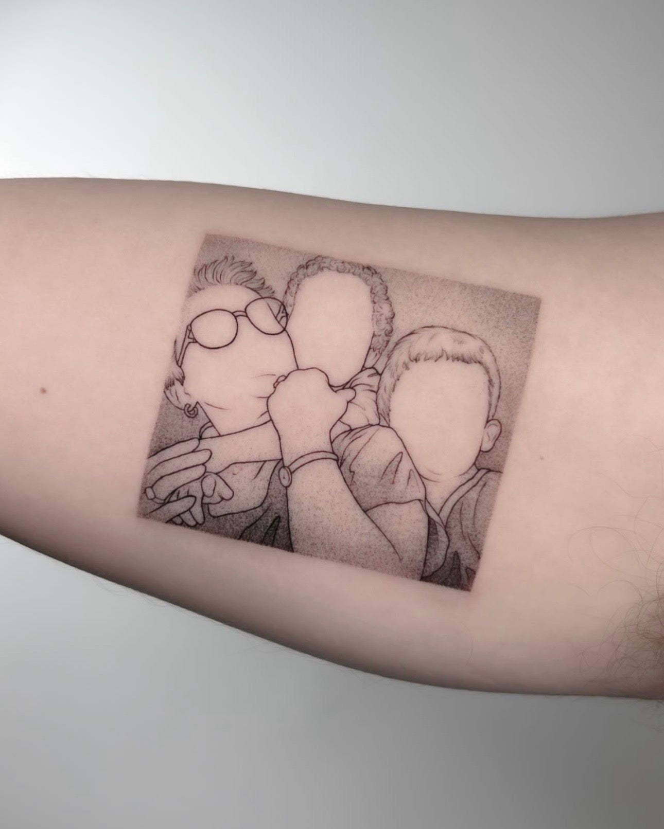 Tatuagem fine line de retrato de família com três figuras em formato de fotografia no braço, estilo ilustrativo minimalista, feita no Dilúvio Tattoo em Benfica, Lisboa.