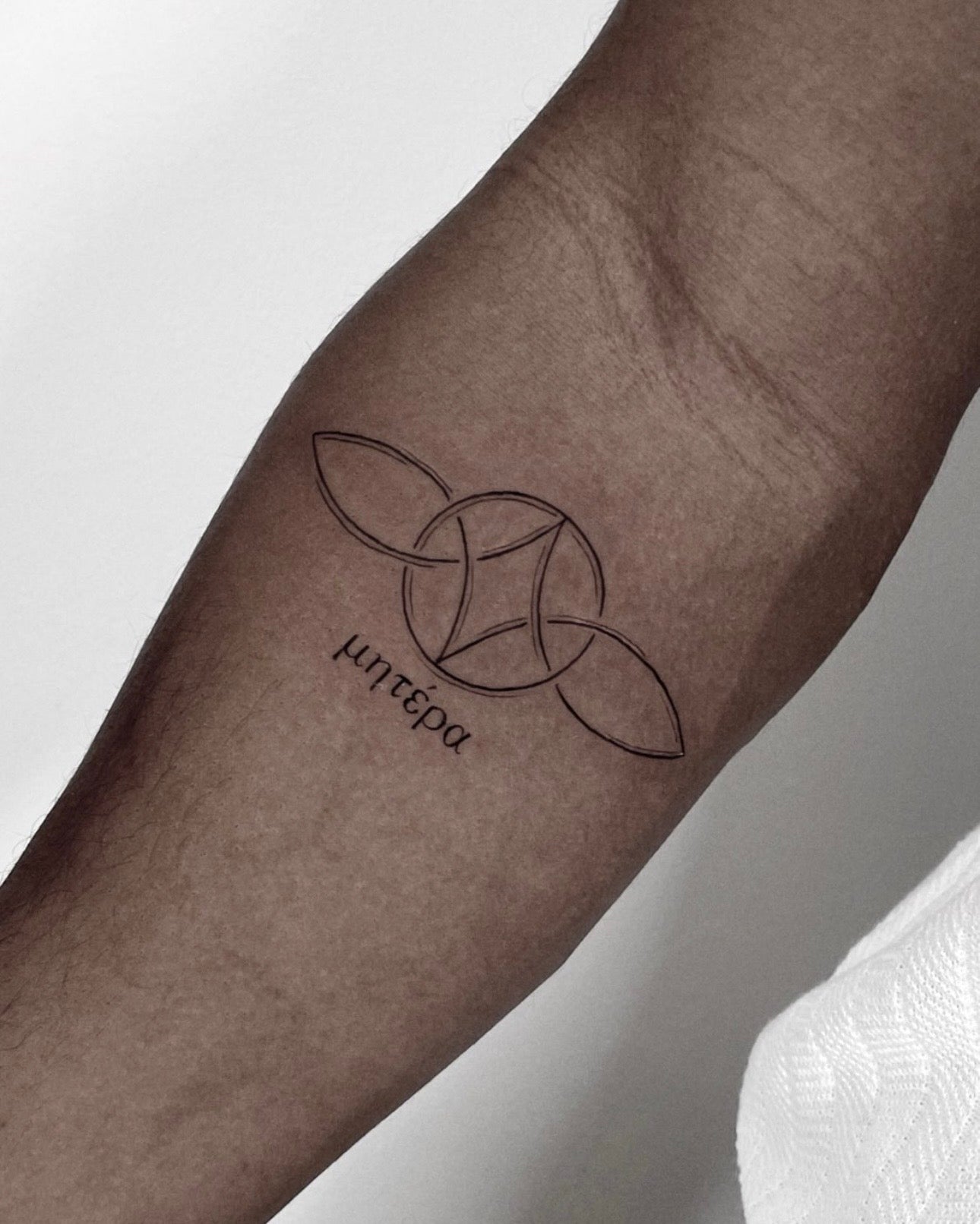Tatuagem fine line de símbolo geométrico com lettering grego 