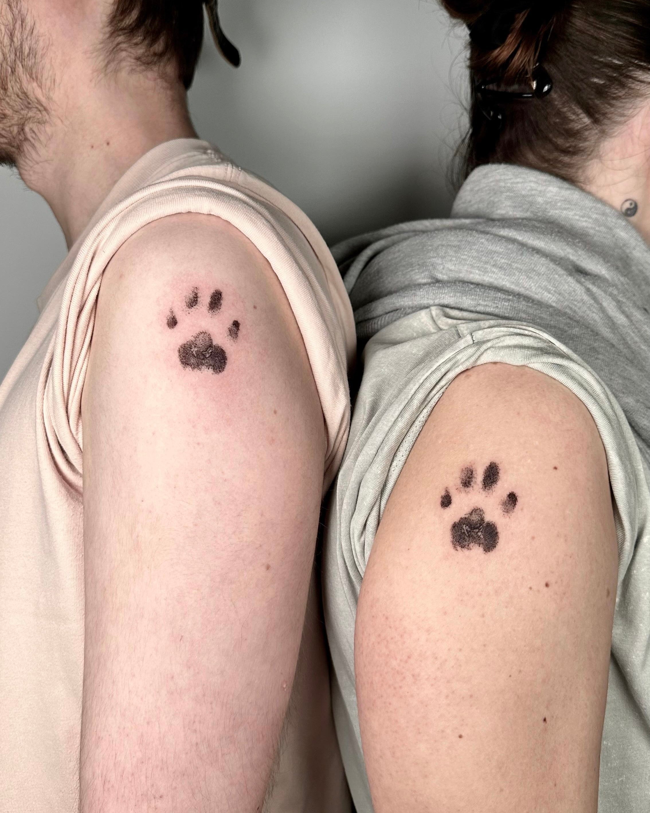 Tatuagens matching de pegadas de patas com sombreado suave nos ombros, homenagem partilhada ao animal de estimação, na Dilúvio Tattoo em Benfica
