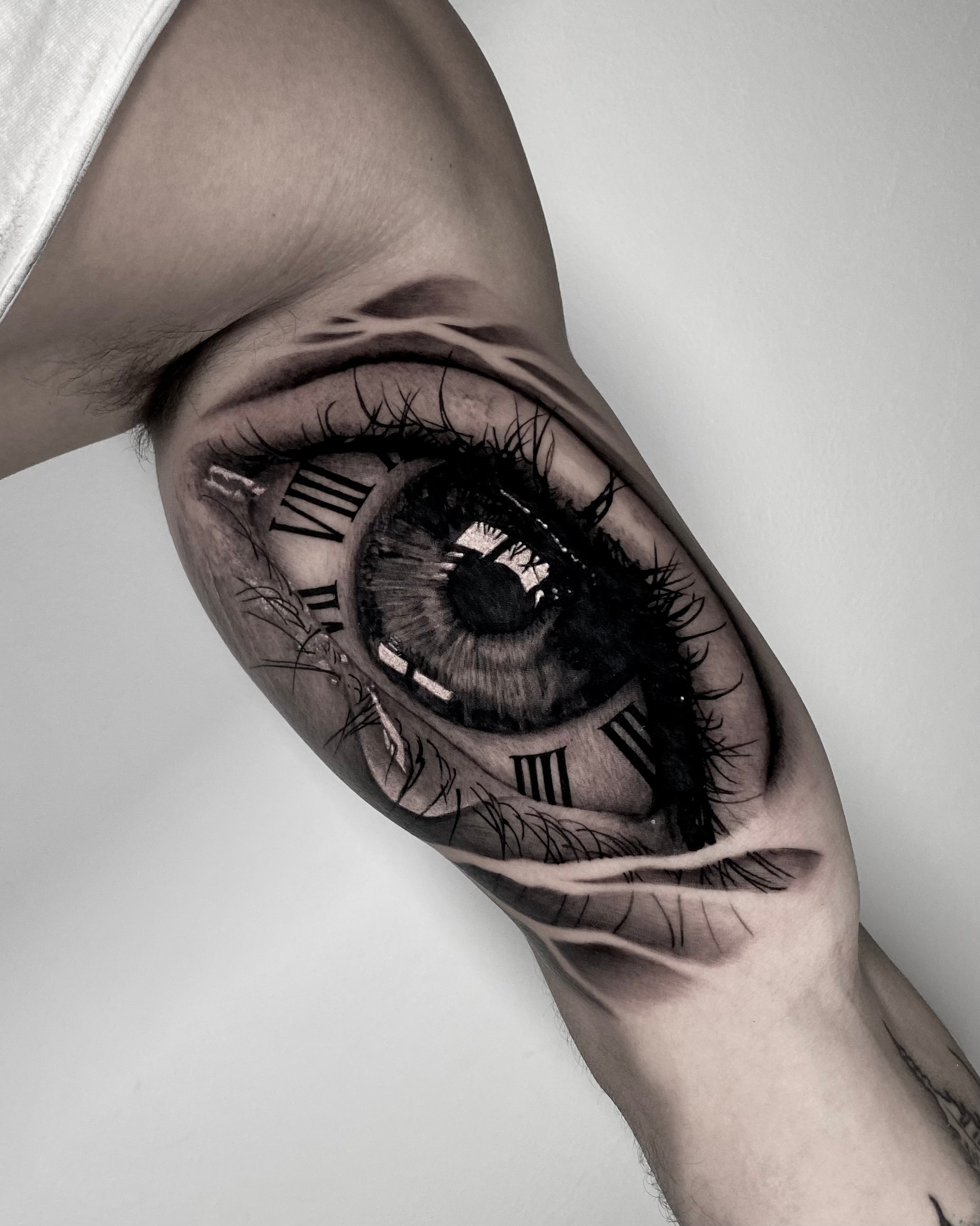 atuagem hiper-realista de olho com algarismos romanos e reflexo detalhado no braço interior, black and grey, feita na Dilúvio Tattoo em Benfica, Lisboa.