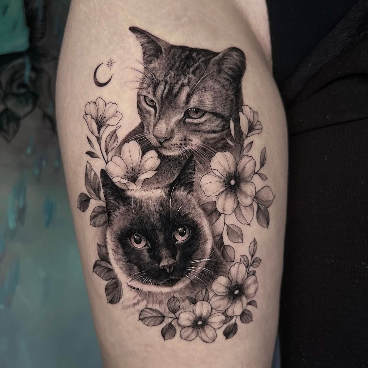 Tatuagem realista de retratos de dois gatos rodeados por flores no braço, black and grey feminino, homenagem a animais de estimação, no Dilúvio Tattoo em Benfica.