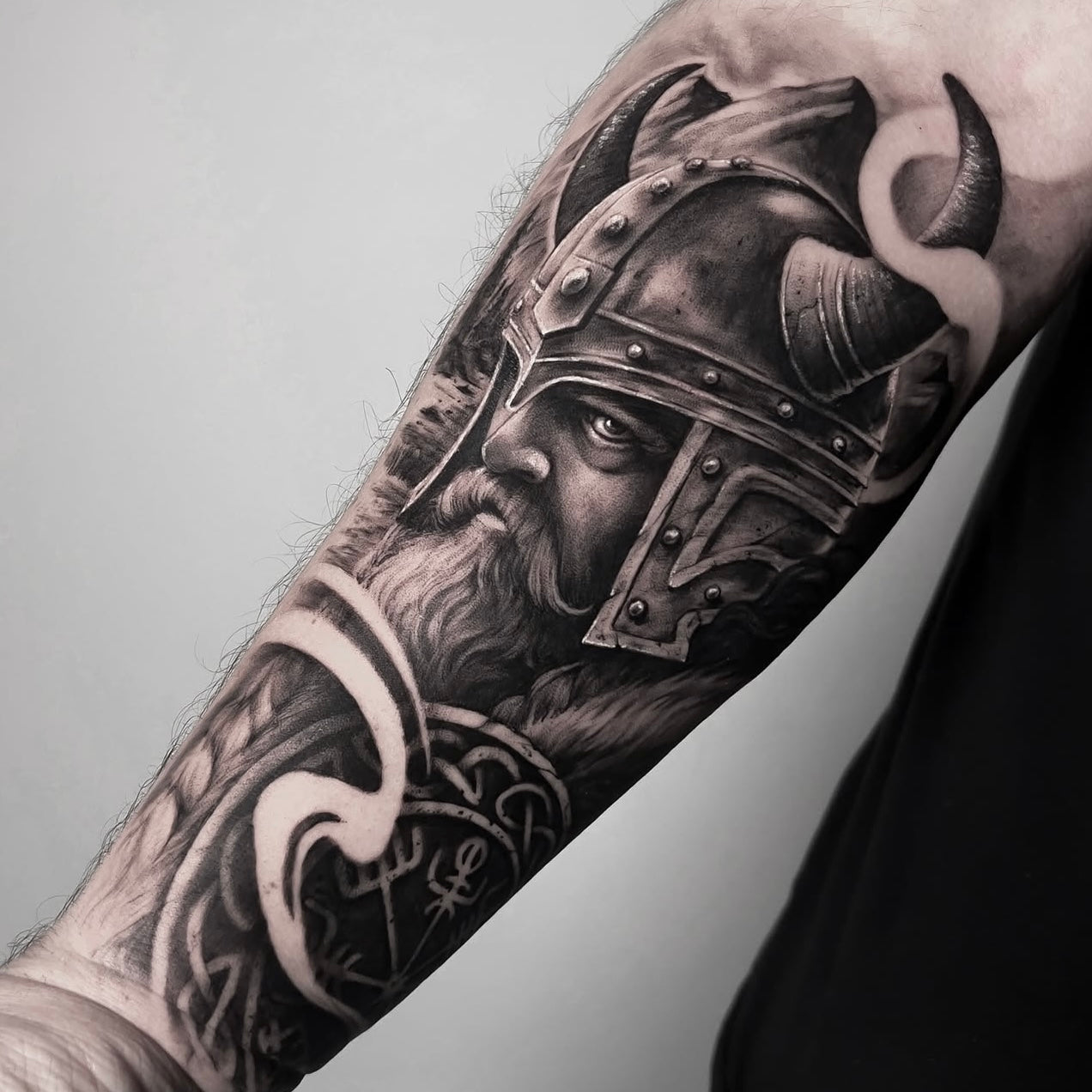 Tatuagem realista em black and grey de viking guerreiro com capacete de chifres e ornamentos nórdicos no braço, feita na Dilúvio Tattoo em Benfica, Lisboa.