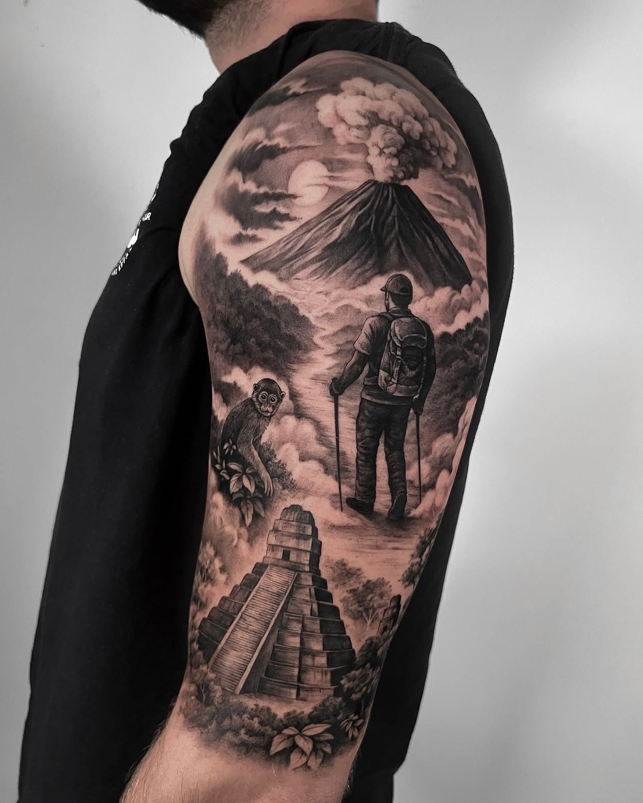 Tatuagem realista em black and grey de vulcão em erupção com montanhista e pirâmide maia no braço, estilo paisagem realismo, feita na Dilúvio Tattoo em Benfica, Lisboa.