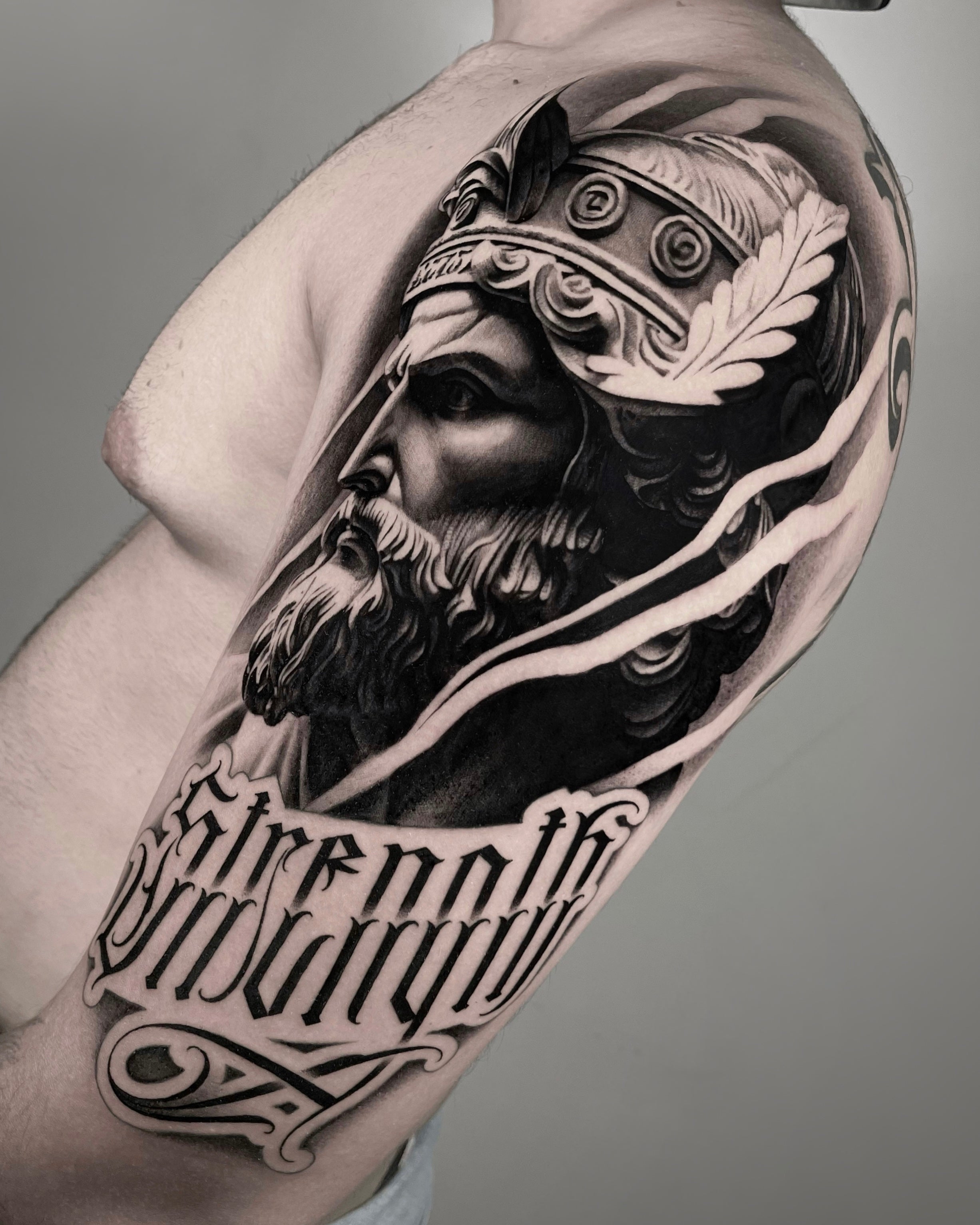 tatuagem em black and grey de figura mitológica grega com coroa de louros e lettering 