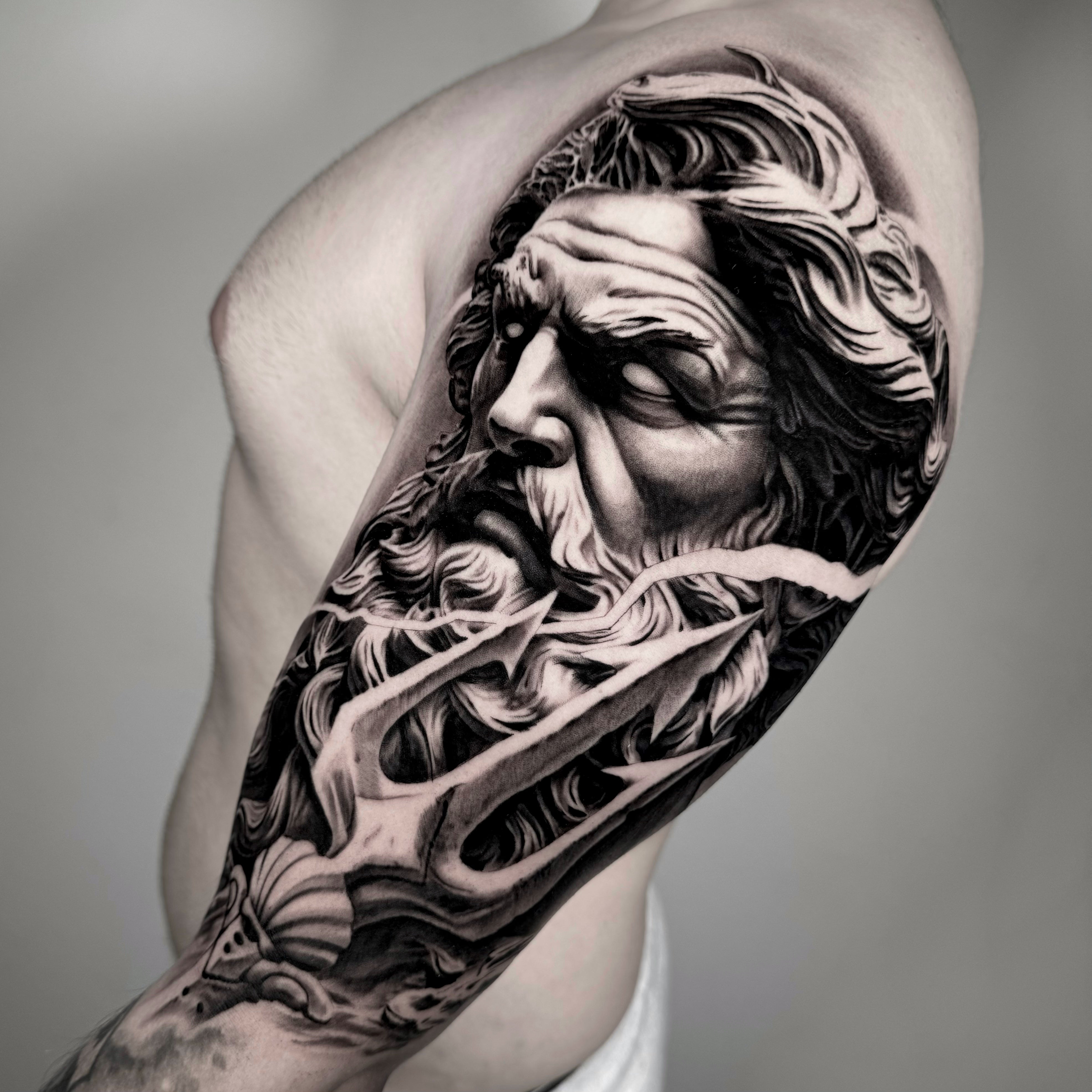 Tatuagem realista em black and grey de Zeus com barba e cabelo esvoaçante no braço, estilo mitologia grega realismo, feita na Dilúvio Tattoo em Benfica, Lisboa